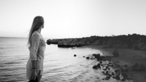 Black and white picture of a woman looking at the horizon on the sea